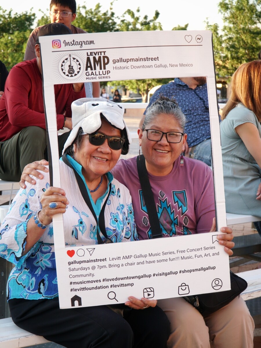 Two women smile while holding a cut-out Instagram photo frame over their faces.