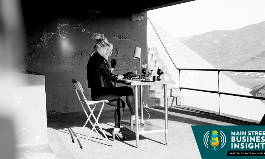Black and white photo of woman sitting at small work table. In the foreground is a graphic that reads "Main Street Business Insights"